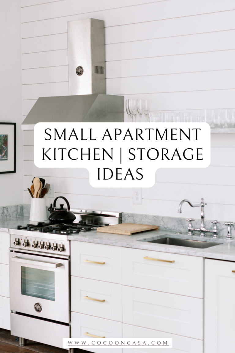 Bright white small apartment galley kitchen with shiplap walls, marble countertops, stainless steel range hood, white cabinets with gold hardware, black kettle, wooden utensils in a white crock, cutting board, and open glass shelving styled for a small apartment kitchen organization and storage ideas post