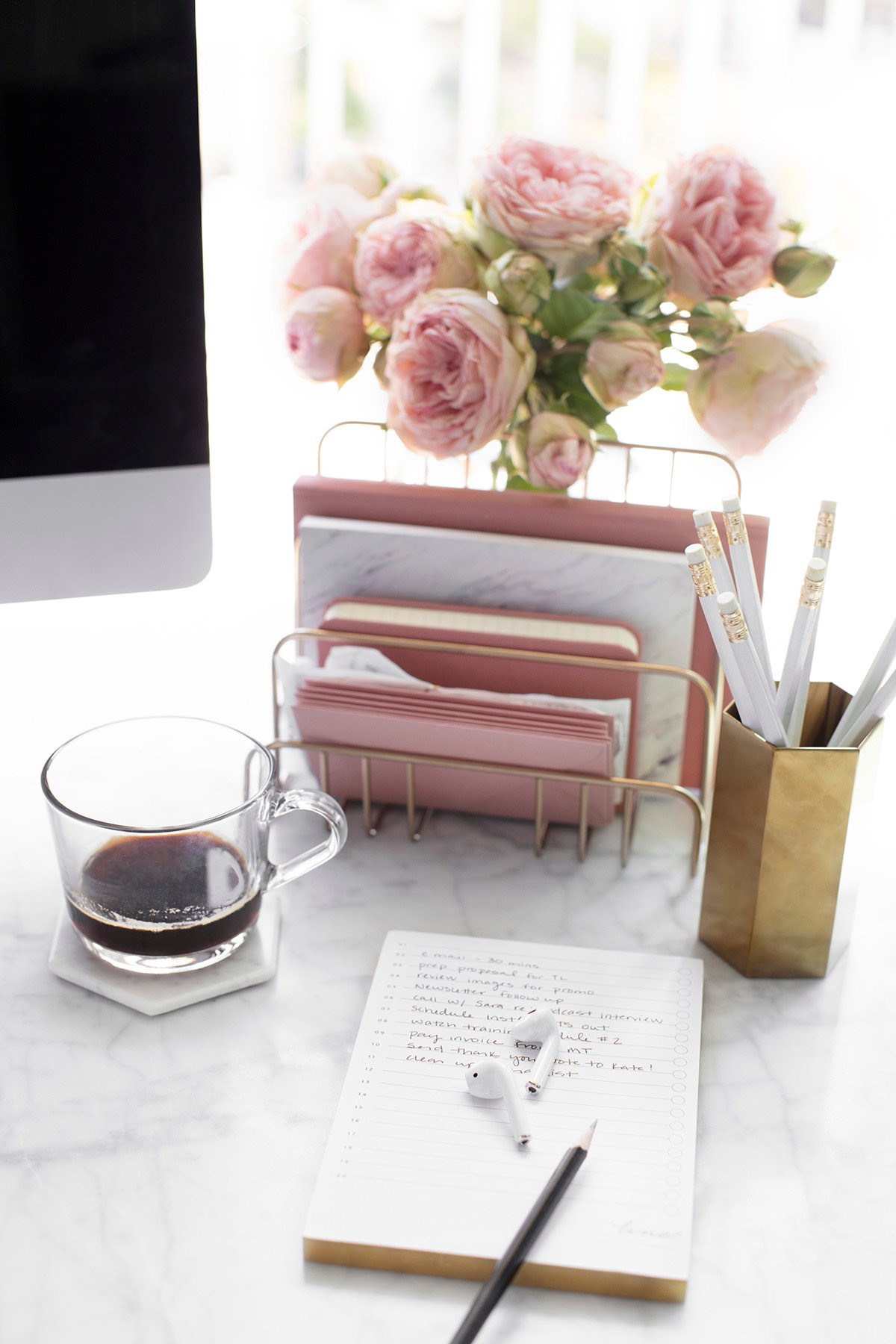 desk with pencil holder with white pencils. gold file organizer, flowers, cup of coffee